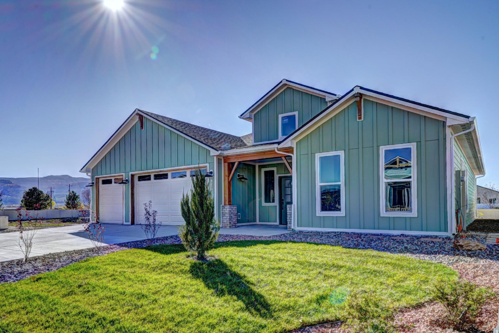 Front view of the Magnolia home featuring a teal exterior, two-car garage, windows, and a landscaped green yard. The image highlights architectural design, color, and curb appeal for residential analysis